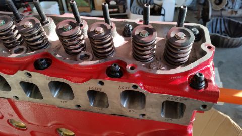 1981 Ford Bronco - Close-up view of the top of a red engine block, showing valve springs, retainers, and studs. Several intake ports are visible on the side o…