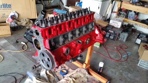 1981 Ford Bronco - A red Ford V8 engine block is mounted on an orange engine stand in a garage. The engine is partially assembled with valve springs visible o…