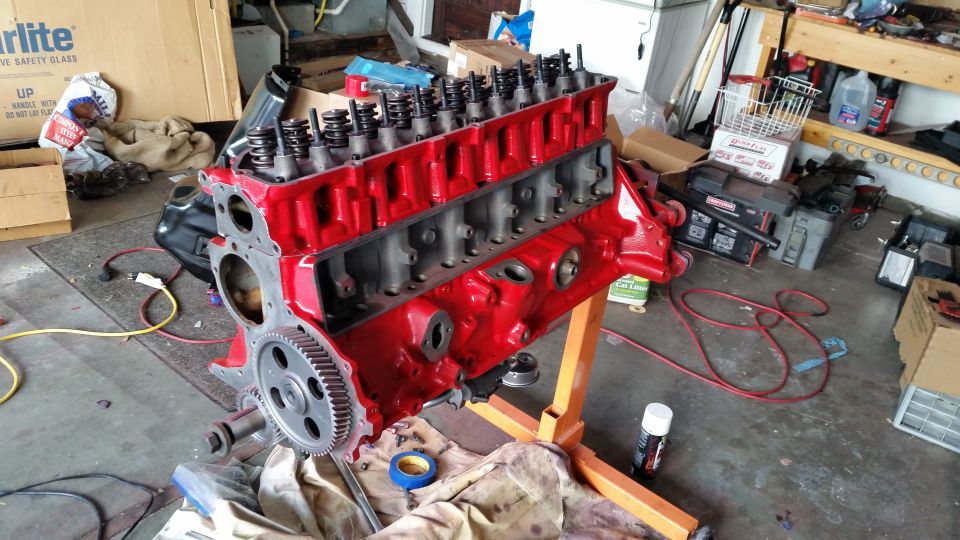 Red Ford V8 engine block on an orange engine stand in a garage, partially assembled.