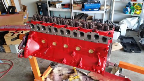 1981 Ford Bronco - A red V8 engine block and cylinder head assembly is mounted on an orange engine stand in a garage setting. The engine appears to be undergo…