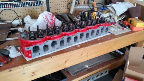 1981 Ford Bronco - A red painted engine cylinder head with visible valve springs and bolts sits on a wooden workbench. The cylinder head has intake and exhaus…
