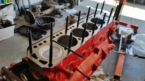 1981 Ford Bronco - A close-up view of a red engine block with pistons installed and cylinder head studs protruding. An Allen wrench is inserted into one of th…