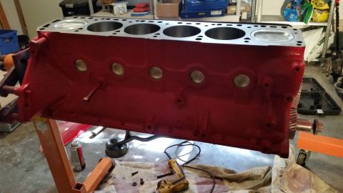 1981 Ford Bronco - A red engine block is mounted on an orange engine stand. The top of the block shows cylinder openings, and the side has circular ports.