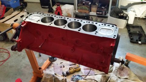 1981 Ford Bronco - A red V8 engine block with pistons installed is mounted on an orange engine stand. The engine block is in a garage setting with various too…