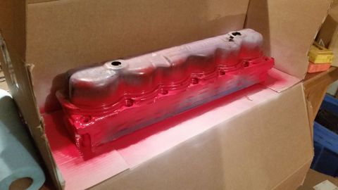 1981 Ford Bronco - A red spray-painted valve cover is resting inside a cardboard box, with a roll of paper towels to the left.