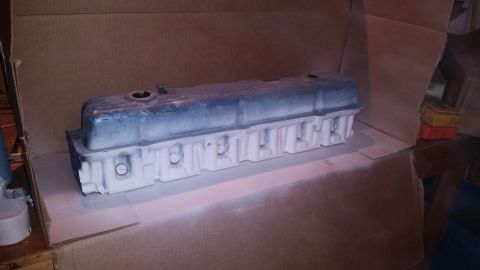 1981 Ford Bronco - A blue and white painted valve cover is placed inside a cardboard box, resting on a piece of cardboard. The valve cover appears to be under…