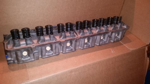 1981 Ford Bronco - A gray engine cylinder head with multiple black valve springs and stems is shown lying on a brown cardboard surface. The cylinder head is v…