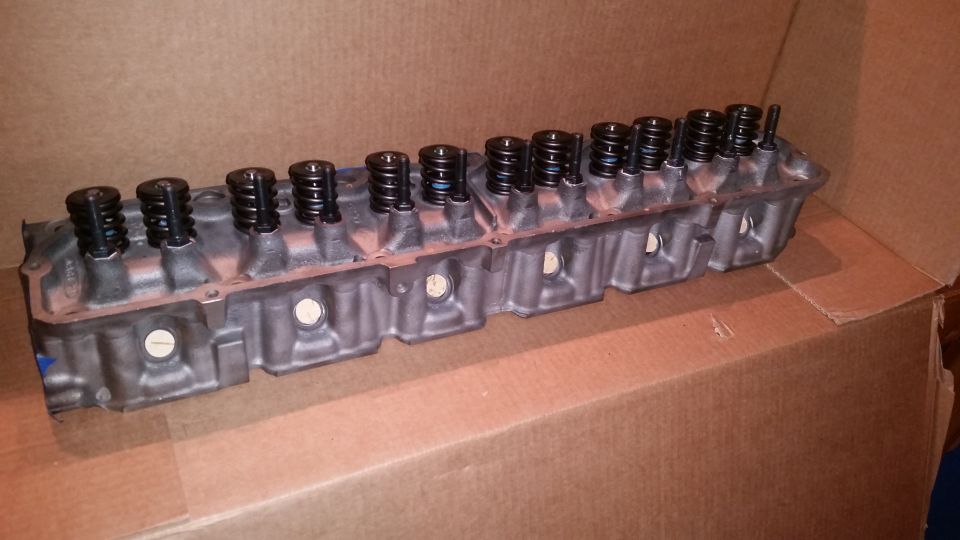 Gray engine cylinder head with black valve springs and stems on cardboard.