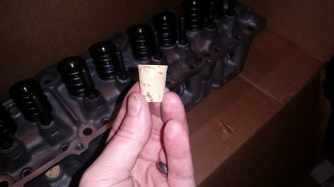 1981 Ford Bronco - A hand holds a small cork stopper in front of a disassembled engine cylinder head. The cylinder head is made of aluminum and has black valv…