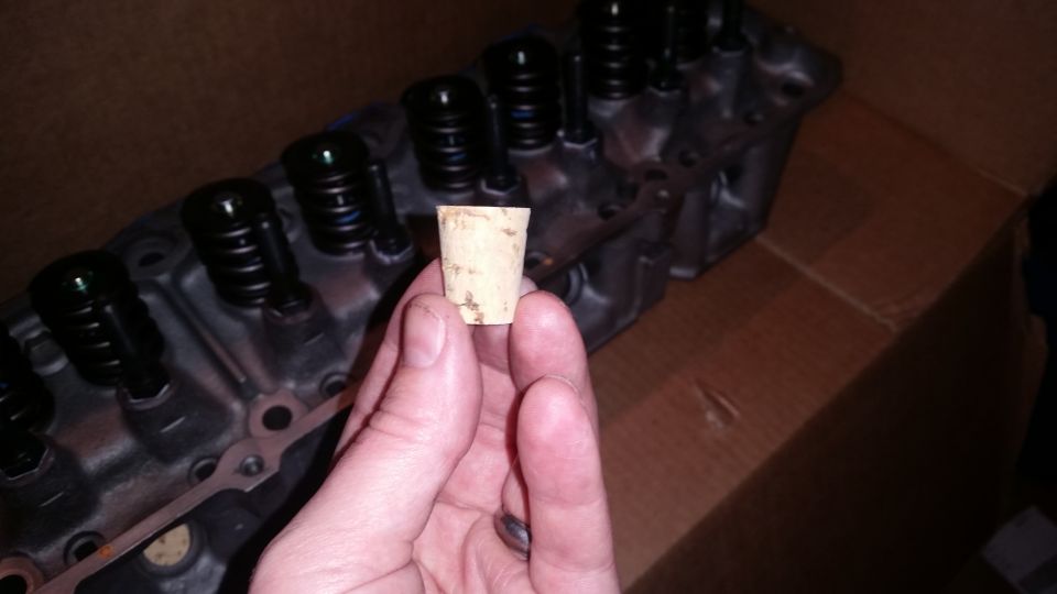 Hand holding a cork stopper in front of an engine cylinder head.