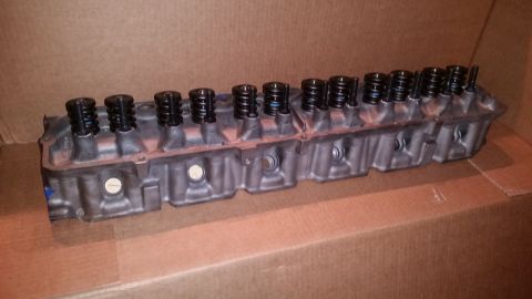 1981 Ford Bronco - A gray engine cylinder head with multiple black valve springs is shown resting on a cardboard surface. The cylinder head has a metallic fin…