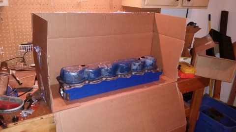 1981 Ford Bronco - A blue engine valve cover is placed inside a cardboard box, resting on a blue block. The valve cover appears to be part of a vehicle build…