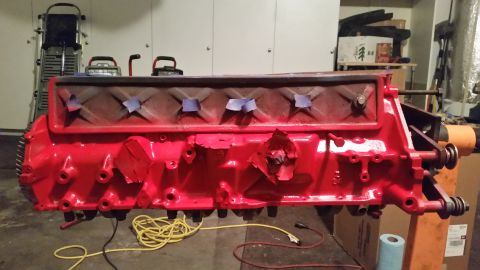1981 Ford Bronco - A bright red engine block is mounted on an engine stand in a garage. Blue tape covers some openings on the top of the engine, and red tape…