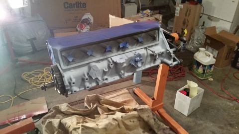 1981 Ford Bronco - A gray engine block is mounted on an orange engine stand and appears to be undergoing some sort of preparation or painting. Blue masking ta…