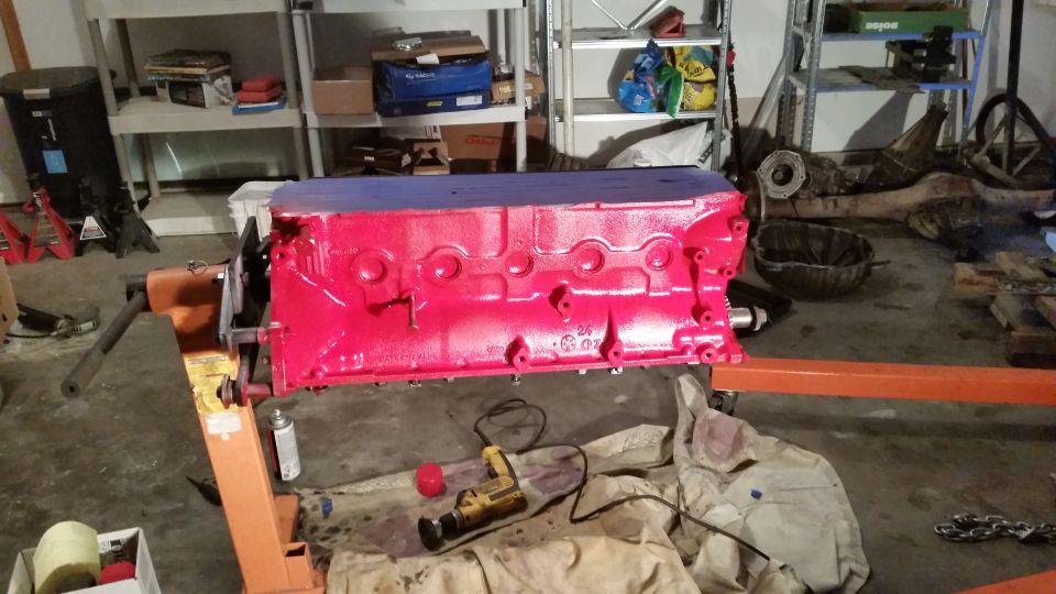 Red engine block on an orange engine stand in a garage.