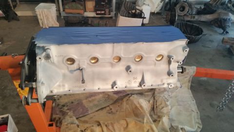 1981 Ford Bronco - A white engine block is mounted on an orange engine stand, with blue painter's tape covering the top surface. The engine block is in a work…