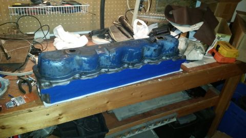 1981 Ford Bronco - A blue engine valve cover is sitting on a wooden workbench, partially covered by a blue mat. Various tools and supplies are visible in the…