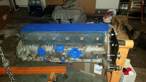 1981 Ford Bronco - A V8 engine block is shown on an engine stand, with blue painter's tape covering the valve cover. The engine is suspended by a chain and ap…
