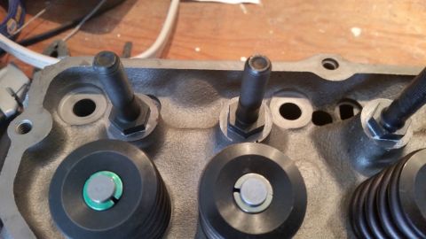 1981 Ford Bronco - A close-up view of the top of a gray metal engine cylinder head, showing two valve spring retainers and two rocker arm studs with hex nuts.…