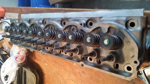 1981 Ford Bronco - A close-up view of a disassembled engine cylinder head with valve springs and retainers installed. The cylinder head is resting on a wooden…