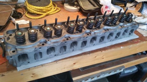 1981 Ford Bronco - A disassembled engine cylinder head with valve springs and retainers installed is resting on a wooden workbench. The cylinder head has visi…