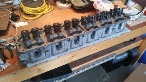 1981 Ford Bronco - A disassembled engine cylinder head with multiple valves and springs is laid out on a wooden workbench. Tools and other workshop items are…