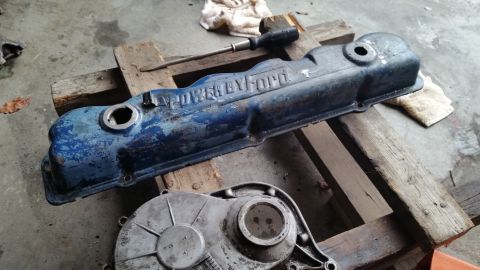 1981 Ford Bronco - A blue Ford valve cover with raised lettering that reads "POWER BY FORD" sits on a wooden pallet next to a silver engine component. A screw…