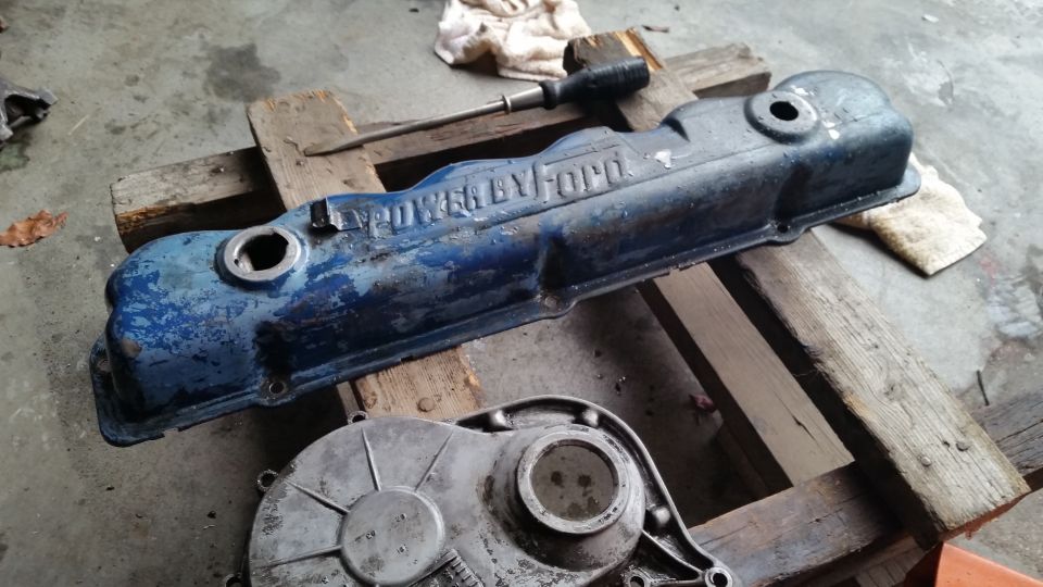 Blue Ford valve cover with "POWER BY FORD" lettering on a wooden pallet.