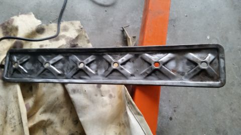 1981 Ford Bronco - A close-up, overhead view of a metal part with a decorative cross pattern and circular holes, resting on a stained cloth next to an orange…