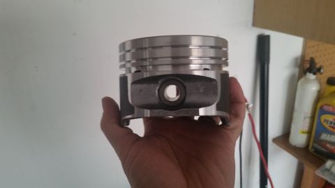 1981 Ford Bronco - A hand holds a piston, likely for a 1981 Ford Bronco, in front of a white wall. The piston is made of metal with distinct grooves at the to…
