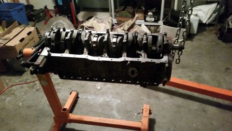 1981 Ford Bronco - An engine block with crankshaft and connecting rods is mounted on an orange engine stand. The engine is suspended by chains from above, sug…