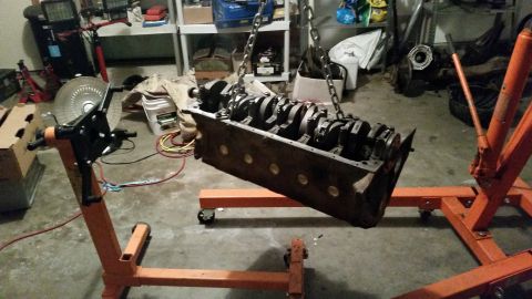 1981 Ford Bronco - An engine block with crankshaft installed is suspended by chains from an engine hoist, resting on an engine stand. The scene appears to be…