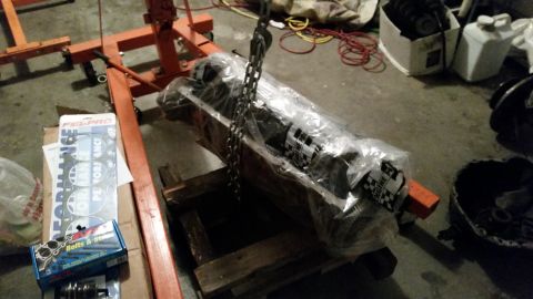 1981 Ford Bronco - Engine block wrapped in plastic and hanging from a hoist, with engine parts nearby.