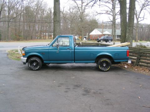 1996 Ford F-150 - A teal pickup truck is parked on a driveway with trees and houses in the background.