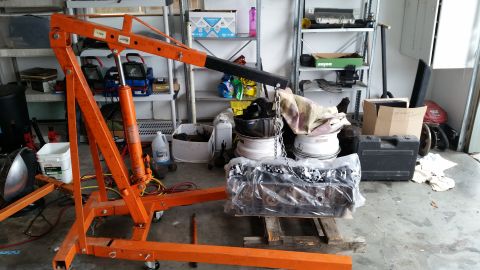 1981 Ford Bronco - An engine block is suspended by an orange engine hoist in a garage setting.