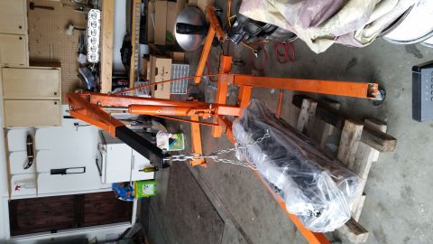 1981 Ford Bronco - An engine is suspended by an orange engine hoist, covered in plastic sheeting.