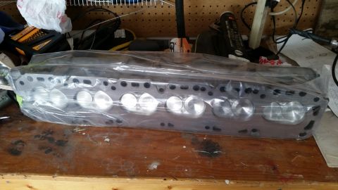 1981 Ford Bronco - Engine cylinder head, wrapped in plastic, sits on a workbench.