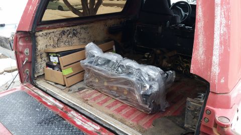 1981 Ford Bronco - Interior view of a red SUV's cargo area, showing an engine block wrapped in plastic and cardboard boxes.