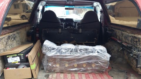 1981 Ford Bronco - The cargo area of a vehicle contains boxes and a large, wrapped item, with a view of the front seats and dashboard.