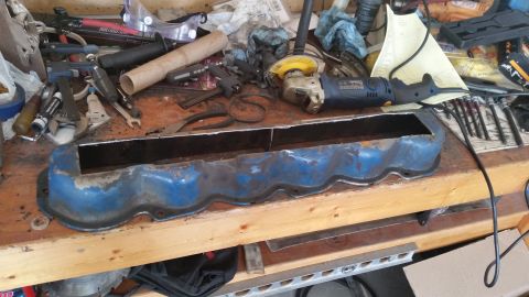 1981 Ford Bronco - A blue valve cover sits on a cluttered workbench surrounded by various tools and equipment.