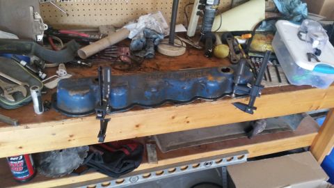 1981 Ford Bronco - A blue valve cover sits on a wooden workbench, held in place by calipers.