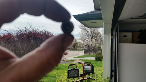 1981 Ford Bronco - A hand holds a small object, obscuring a view of a suburban street and garage.