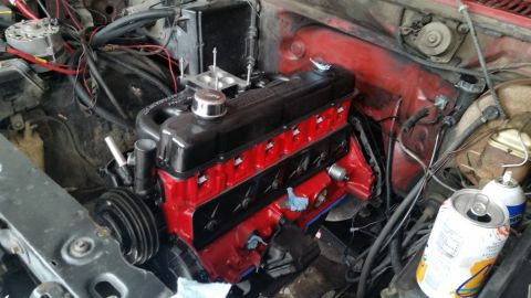 1981 Ford Bronco - Engine bay with a red and black engine, carburetor, and various hoses and wires. A can of spray paint and an open soda can are visible.