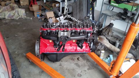 1981 Ford Bronco - A red engine block with black valve covers is suspended by chains on an orange engine stand in a garage.