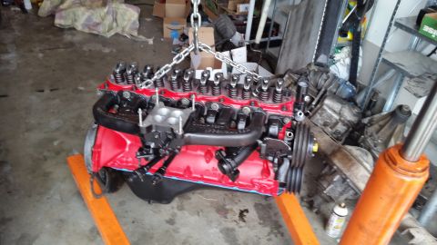 1981 Ford Bronco - Engine assembly, painted red and black, is hoisted by chains in a garage setting.