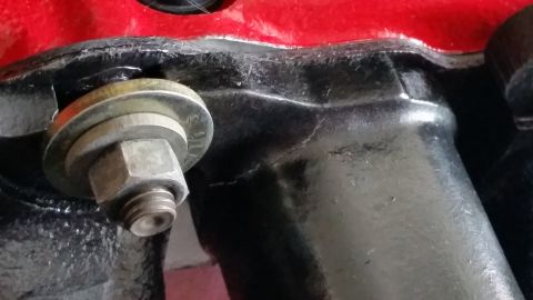 1981 Ford Bronco - Bolt and washer on a black engine part, with a red painted surface visible.