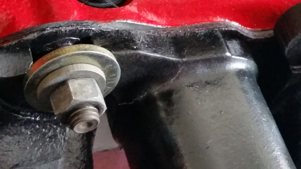 Close-up of a bolt and washer securing a black engine component, with a red surface above