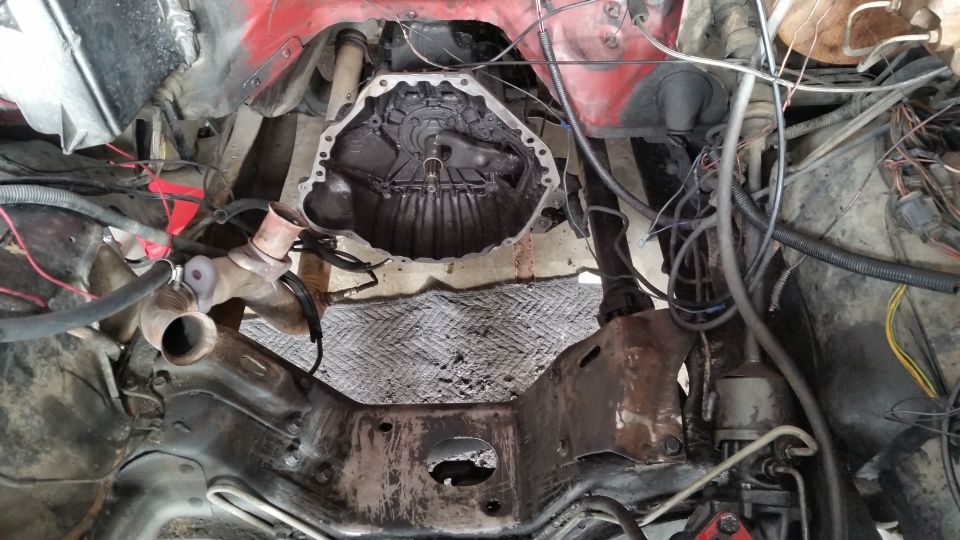 Underside view of a vehicle's engine bay showing the transmission bell housing area, with various hoses and wiring visible