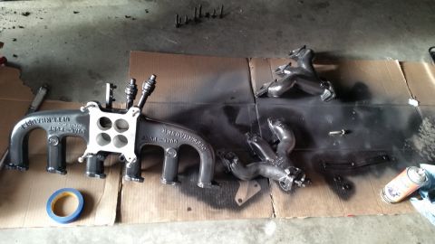 1981 Ford Bronco - Engine parts, including an intake manifold and exhaust manifolds, are laid out on cardboard, possibly for painting.