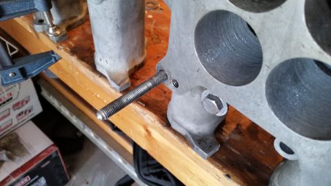 1981 Ford Bronco - A metal engine component is secured with clamps to a workbench for repair or modification.